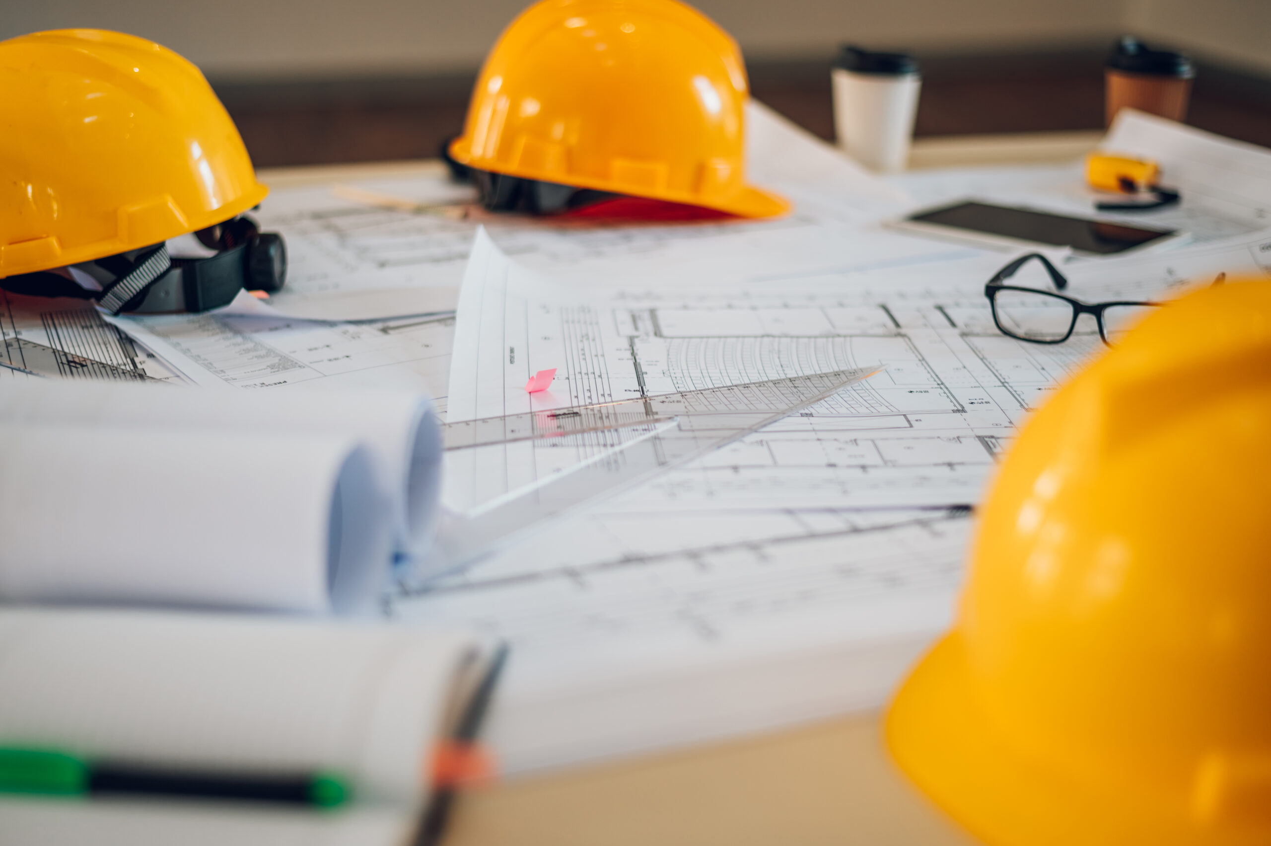 Safety helmets and blueprints laying on the engineering desks. Protective wear helmet hat on desk at construction site. Engineering tools concept. Focus on a building sketch plan.